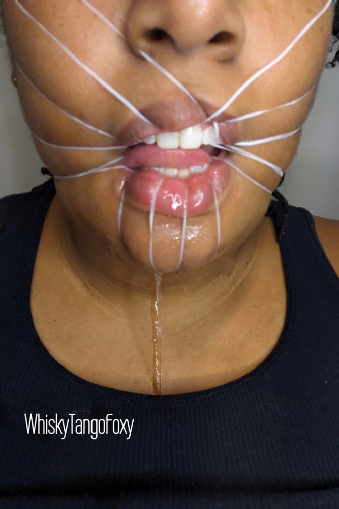 A Black Woman has used dental floss through her teeth to tie her mouth open with significant drool down her chin