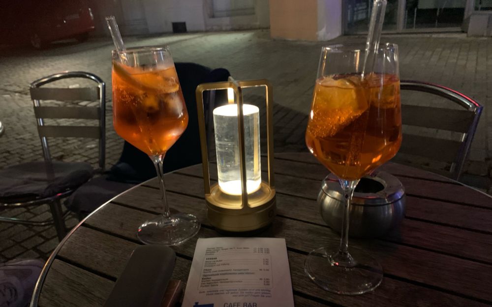 Zwei Gläser Aperol Spritz auf einem Bistrotisch , es ist dunkel ein Licht beleuchtet den Tisch. 