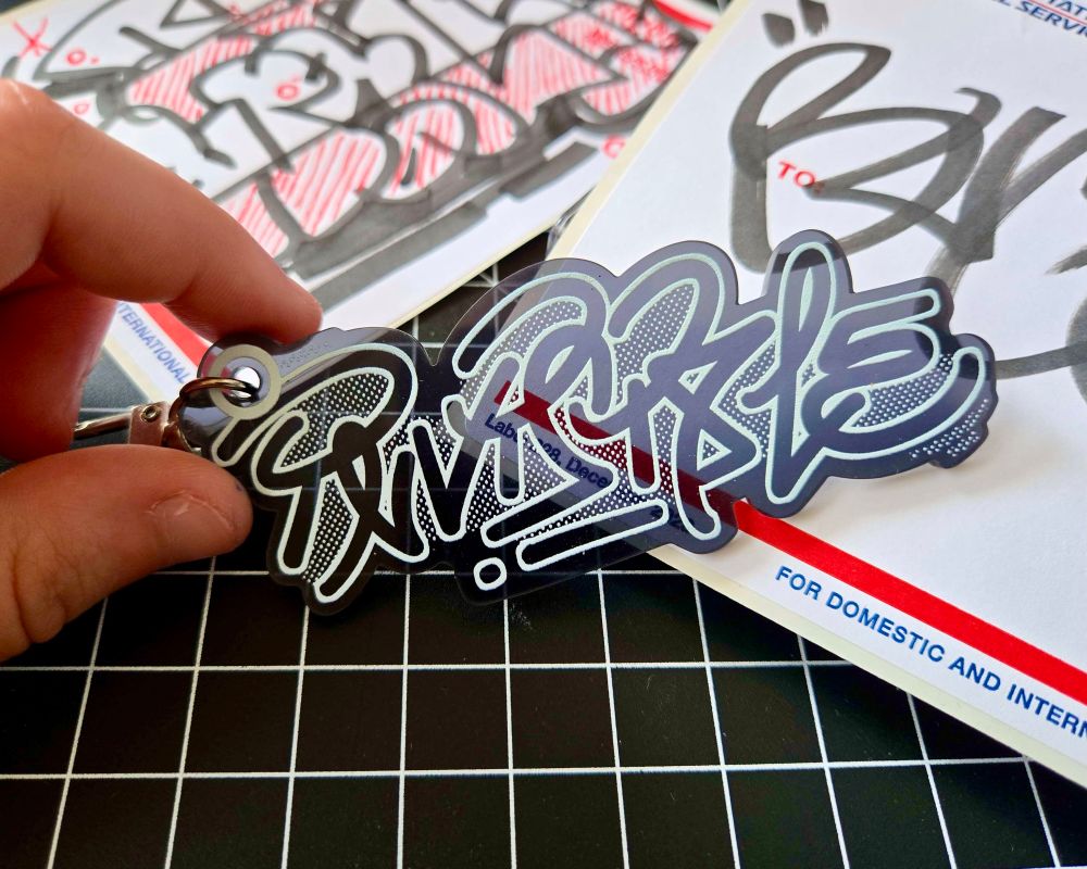 grey graffiti keychain that reads INVISIBLE, by BUGSLAP