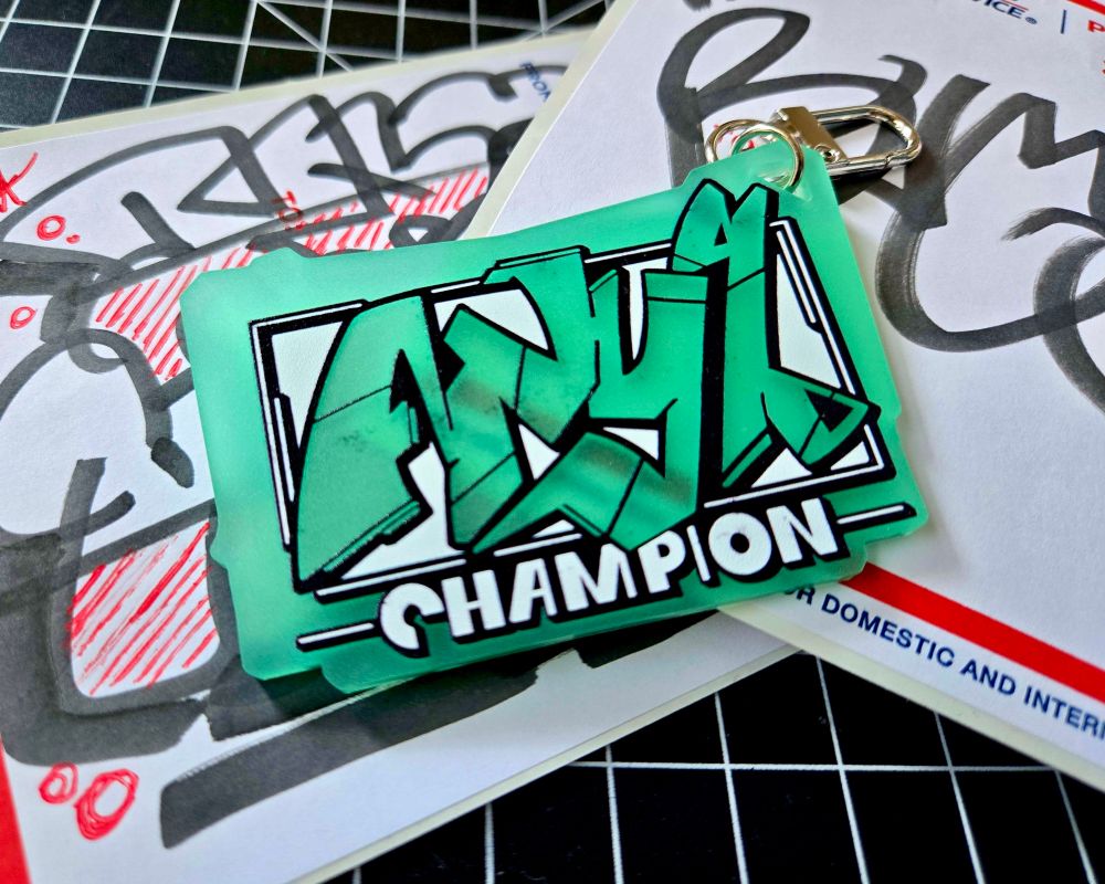 green/blue graffiti keychain that reads "Any% Champion"