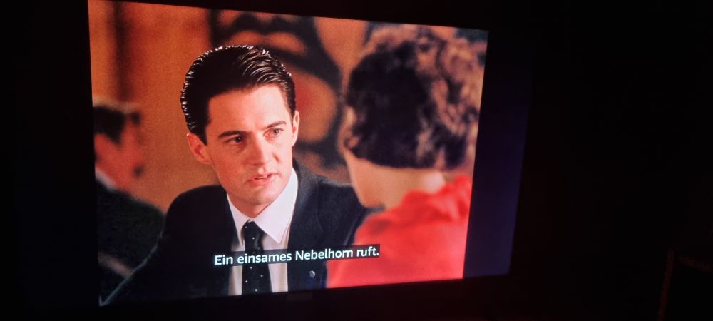 A screenshot of Twin Peaks with subtitles reading "ein einsames Nebelhorn ruft."