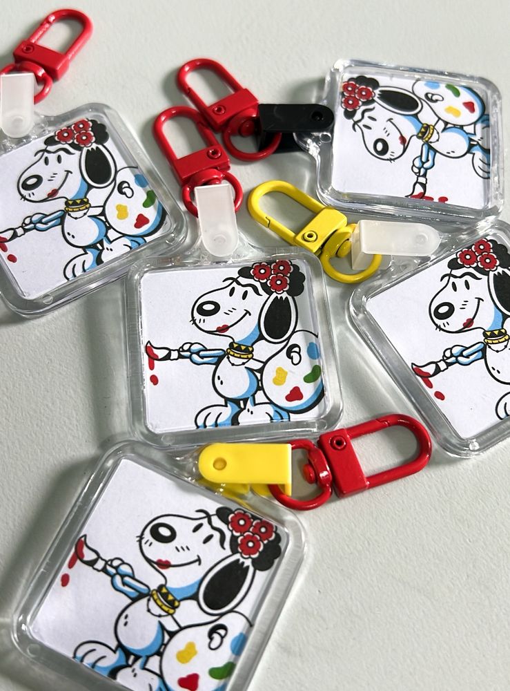 foto de chaveiros com fanart do Snoopy Frida Kahlo, ele está segurando um godê e um pincel sujo de tinta vermelha