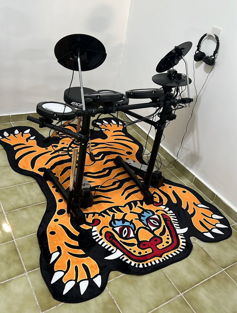 foto de arquivo pessoal, na foto uma bateria eletrônica preta com branco em cima de um tapete de tigre laranja