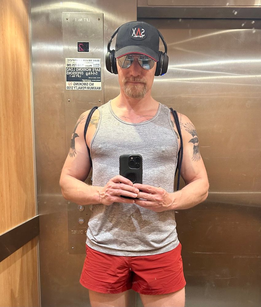 Mirror selfie of Timo in red gym shorts, grey singlet and SAX Fetish cap. 