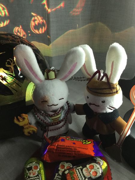 Photograph of two plush bunny keychains, one dressed as Gojyo from Saiyuki and the other dressed as Kami-sama from Saiyuki, with a pile of Reese's candy in front of them and spooky Halloween lights behind them.