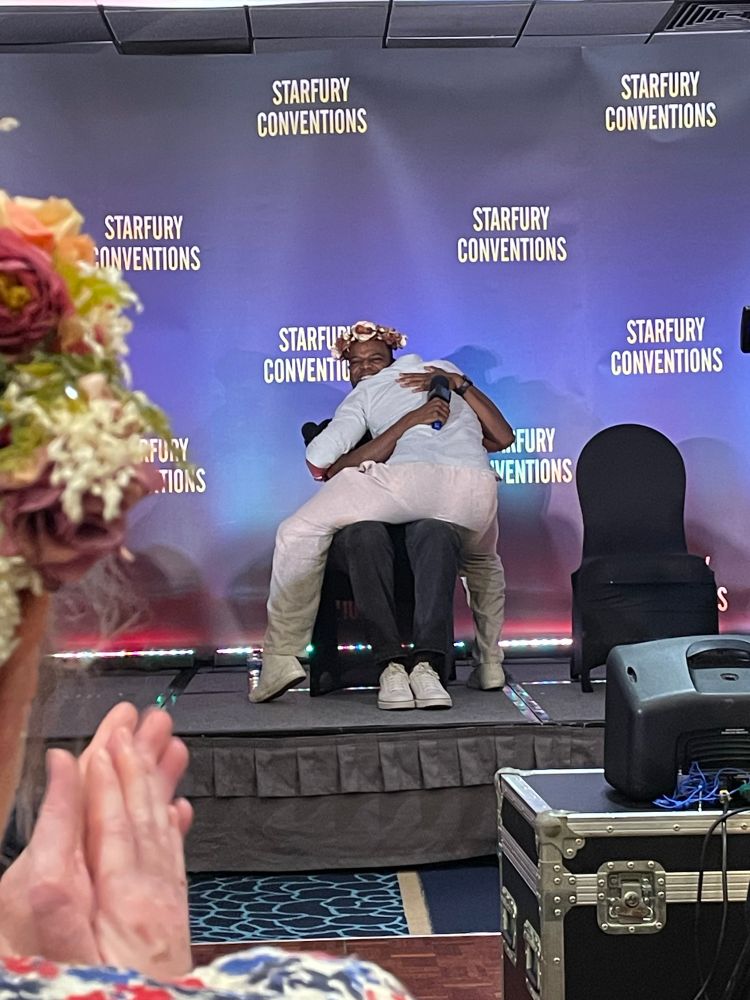 Ricky body hugging a sitting Demore on stage
