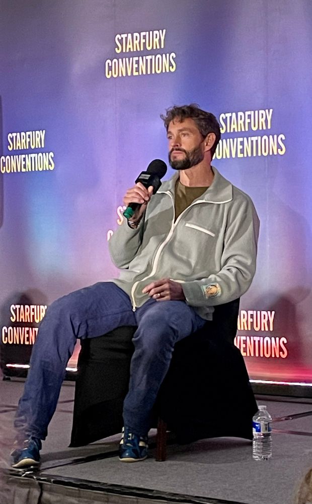 Hugh Dancy seated alone on stage