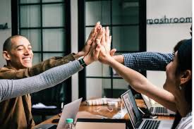 People in a meeting sitting around a table and doing a group high five over the center of the table. Their business endeavor has been successful. 