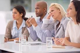 A business meeting were people appear to be either confused, distracted, focused, or skeptical.