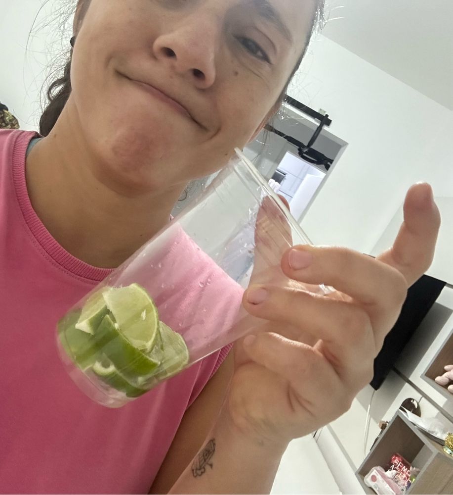 Eu com um sorriso maroto segurando um copo plástico transparente cheio de limão cortado no formato de caipirinha