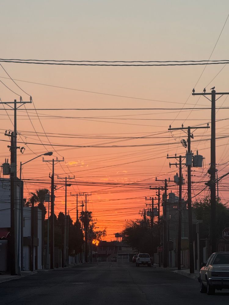 Sunrise with a street that has a lot of cable power lines running accross from post to post