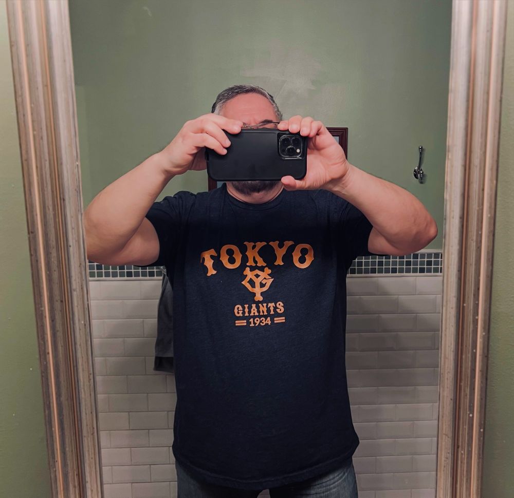 A mirror-selfie of a middle aged dude wearing a blue t-shirt that reads "Tokyo Giants 1934" in orange letters. The team's "YG logo" in the middle of the shirt.