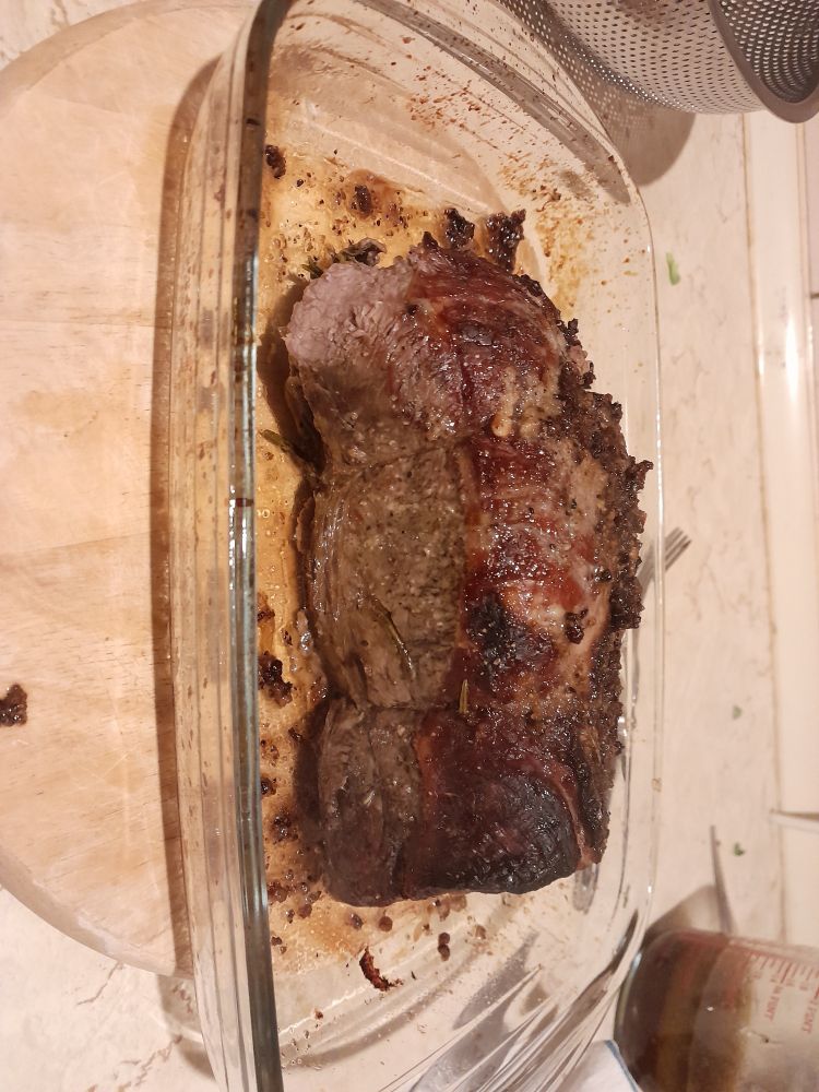A slab of roast beef in a glass dish on a light wood board.