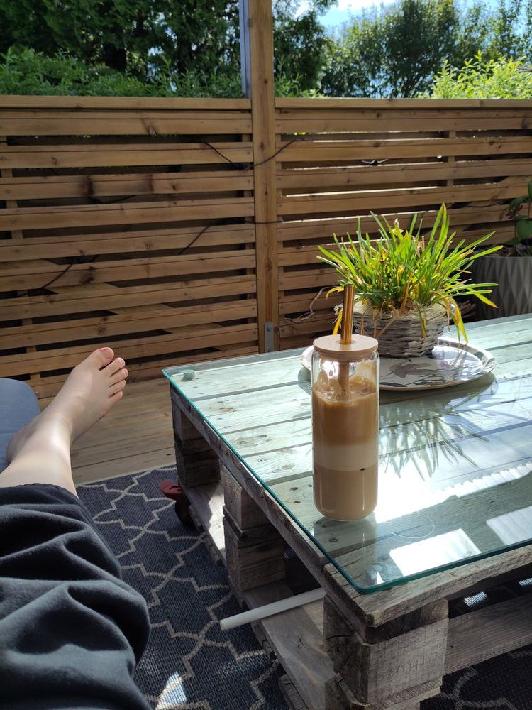 picture of a barefoot and a greek frappe (iced coffee) on a pallet table. with greenery in the background and a blue sky