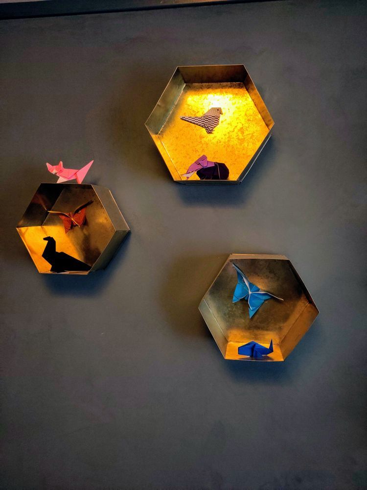photo of a matte blue wall with brass shelves had origami figures in, on top and on the walls of the shelves..there are origami butterflies, cat, mammoth, birds etc. in various colours.