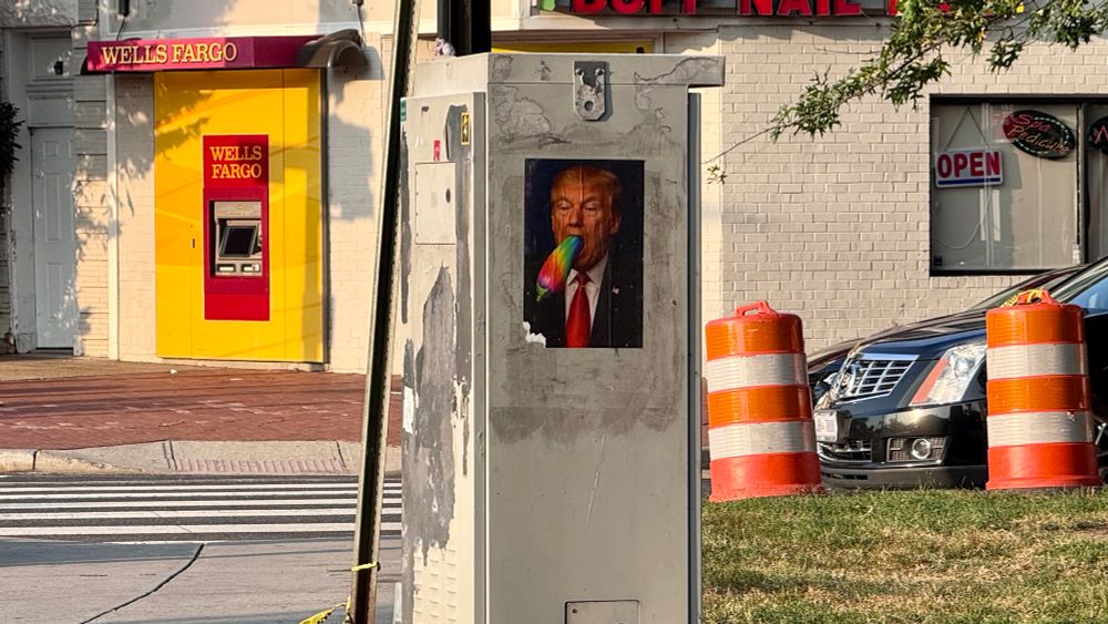 A photo on a utility box on the street on Pennsylvania Ave SE in Washington DC of Donald Trump with a rainbow colored egg plant sliding into his mouth.