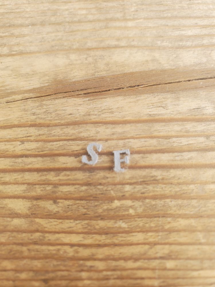 A tiny S and broken E that looks like an F on a light wood surface.