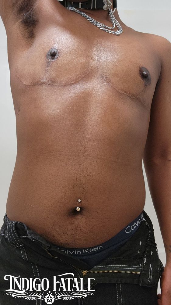 Indigo's glowing, oiled up chest while one arm is up so its hairy armpit is visible. Its black jeans are unbuttoned and showing the top of its Calvin Klein underwear. 