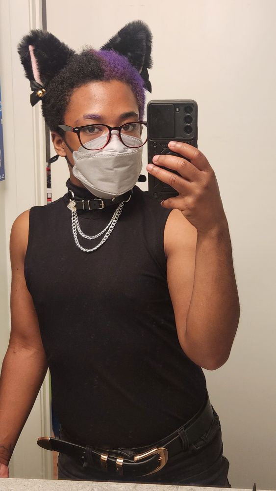 Indigo is wearing black cat ears with bells, a grey mask, glasses, and a sleeveless black top with a choker and layered silver chains in a mirror selfie.