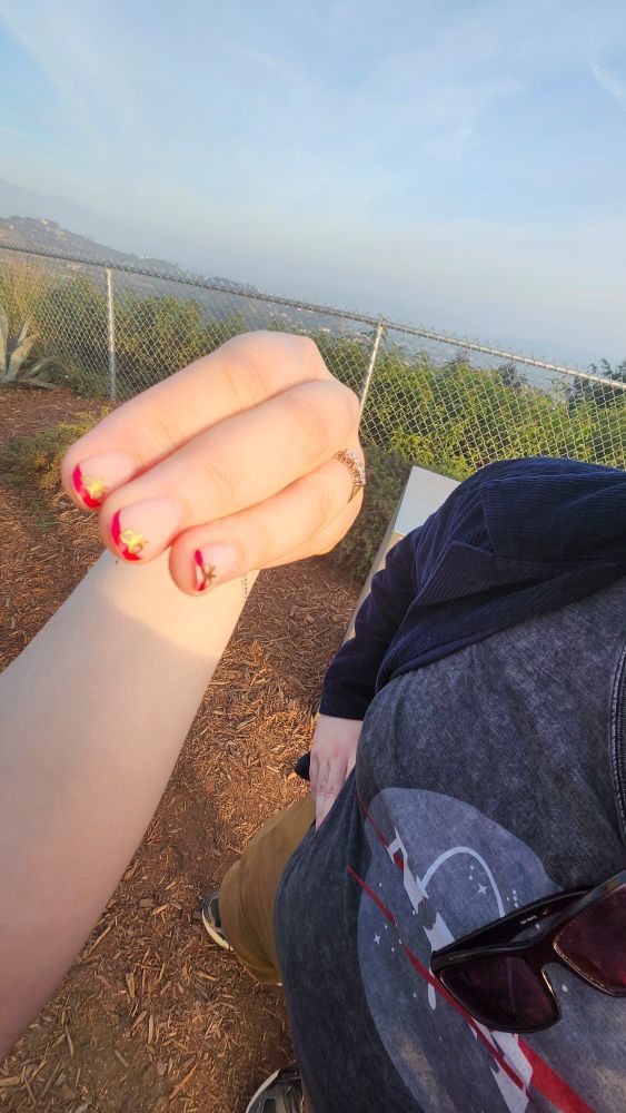 Cursed ass picture of Becca's hand with an engagement ring on it. The picture is on 0.6x Zoom, and only 3 manicured fingers are visible. Nate stands in the background with his hands on his hips.