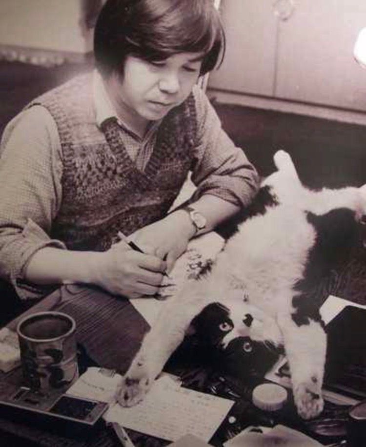 原稿を執筆する赤塚不二夫の机の上にバンザイして寝っ転がる猫の菊千代の写真。