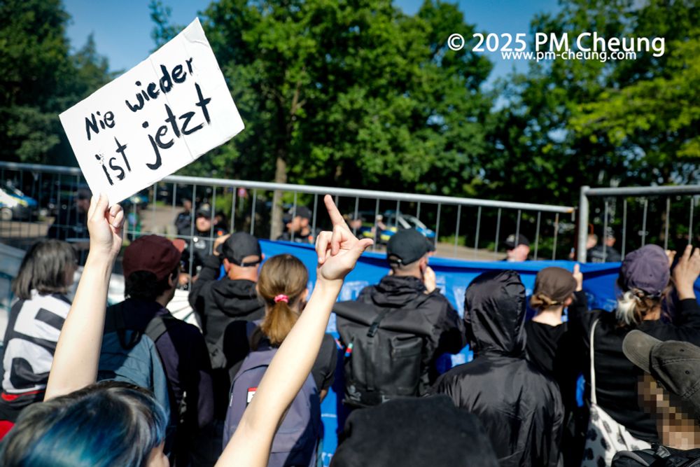 Am Bürgerhaus standen sich die Gegendemonstrant*innen und die Delegierten der AfD gegenüber. Eine Demonstrant*in reckt ein Schild mit der Botschaft "Nie wieder ist jetzt" in die Luft. Gleichzeitig zeigt sie auch ihren Mittelfinger in Richtung der AfD.