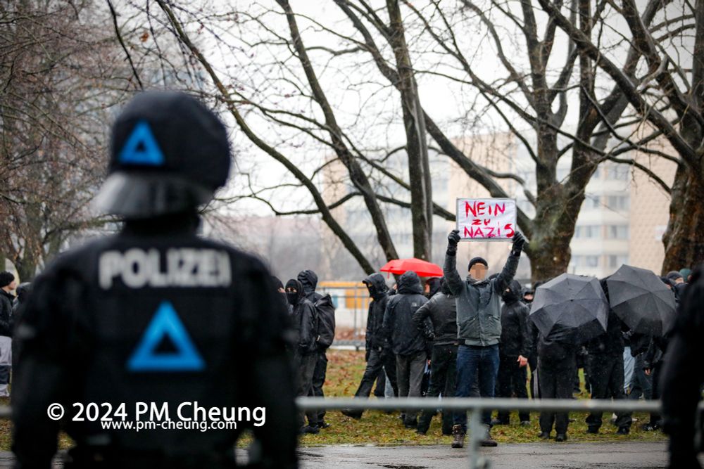 Ein einzelner Demonstrant mit einem "Nein zu Nazis" Schild. Dahinter eine Gruppe autonomer Antifaschist*innen.