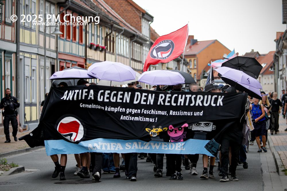 Die Demonstrant*innen auf der Westermarktstraße, ziehen in Richtung Autonomes Zentrum (AZ). Auf dem Frontbanner steht "Antifa gegen den Rechtsruck. Gemeinsam kämpfen gegen Faschismus, Rassismus und Antisemitismus!". Zudem ist eine Fahne der Antifaschistischen Aktion zu sehen, ebenso viele aufgepannte Regenschirme.