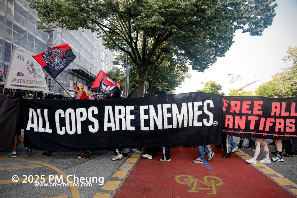 Die Demonstrant*innen passieren die Reeperbahn, dabei wird ein Banner mit der Aufschrift "All Cops are Enemies" und ein weiteres mit "Free all Antifas" gezeigt.