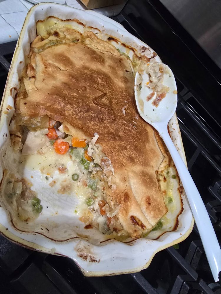 Chicken pot pie in a casserole dish. A section in the lower left corner has been removed. 