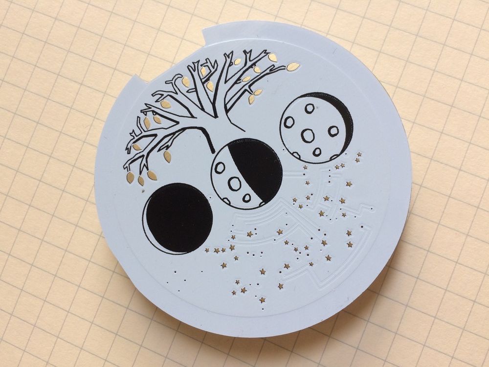Picture of a PCB without any visible components.  There are three phases of the moon, a tree with golden leaves, and a set of stars