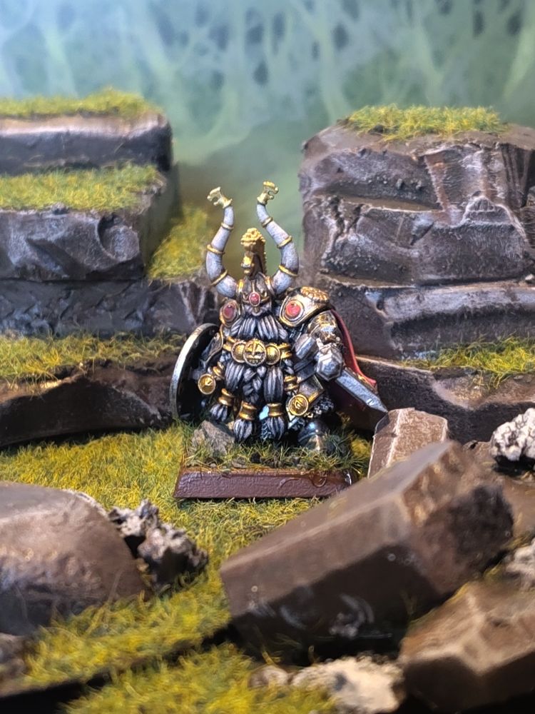 Figure of a Dwarf Lord in heavy armour with an axe and shield standing amidst rocks. 