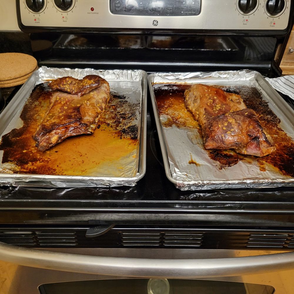 Two racks of lamb ribs resting in baking trays  on the stove top. They are golden brown after coming out of the oven.