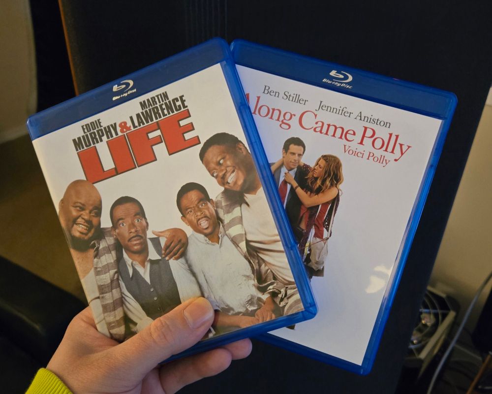 A hand holding fanned Blu-ray cases of "Life"(1999) and "Along Came Polly" (2003)