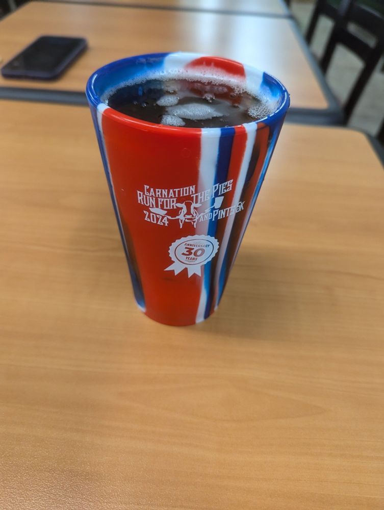 A red white and blue striped cup with beer inside on a table.