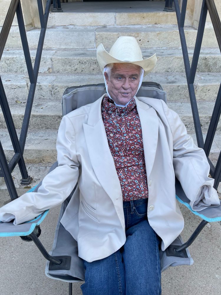 Life-size caricature of representative John Carter of the Texas 31st District. He was made wearing a pair of flare jeans, a flowered long sleeve country style button up shirt, a beige off-white suit jacket, and of course, his signature cowboy hat. His head is made of a paper face cut out on and secured onto foam backing. We sat him in a grey lawn chair. He is seated in front of the Bell county courthouse steps.