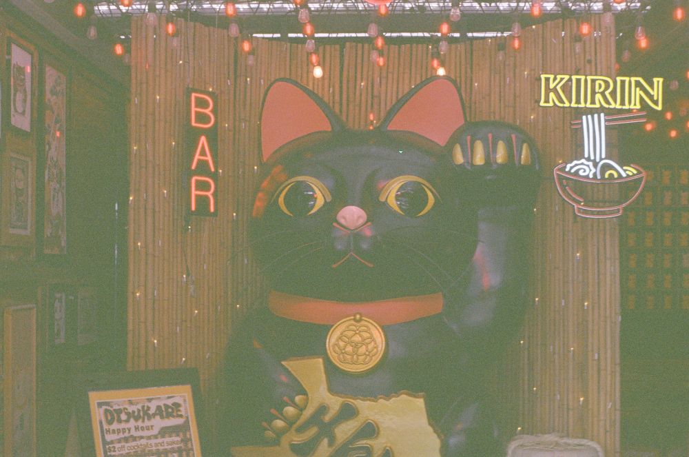 Hazy expired film; giant lucky Cat with neon bar signed to left and neon kirin sign to right
