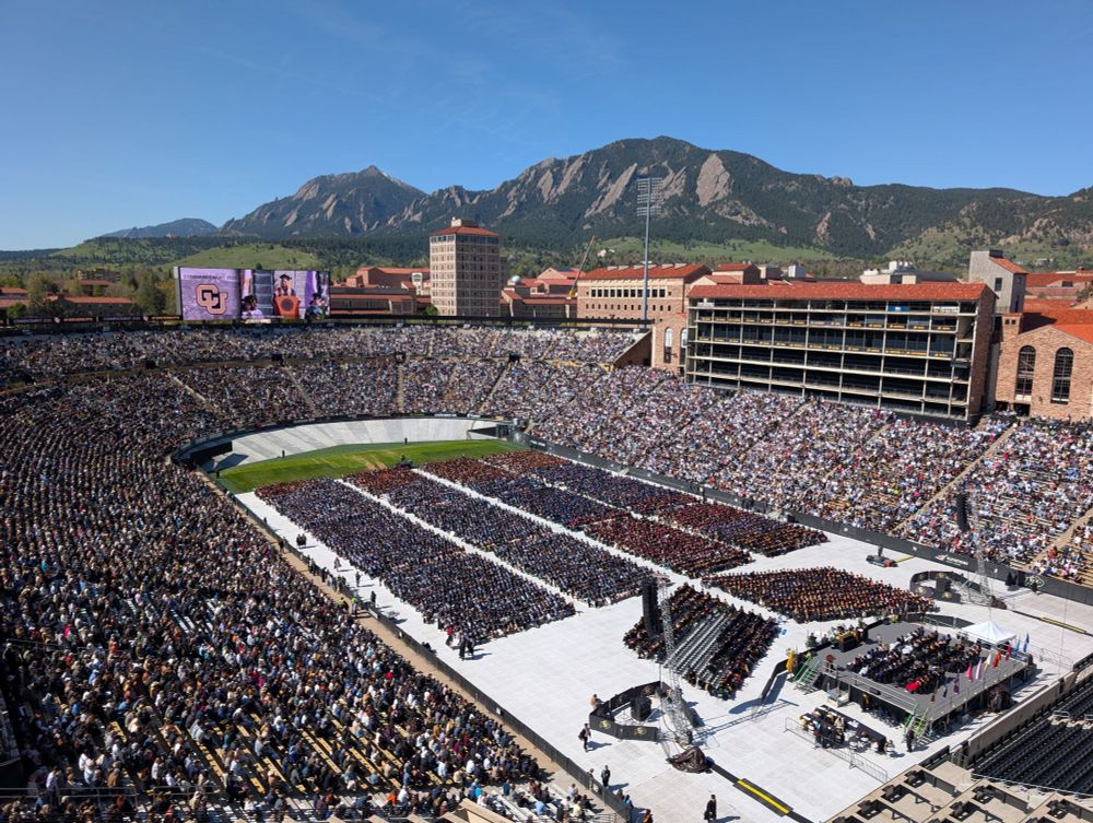 Folsom Field filled with 2025 graduates and their families. Blue sky and the Flatirons in the background