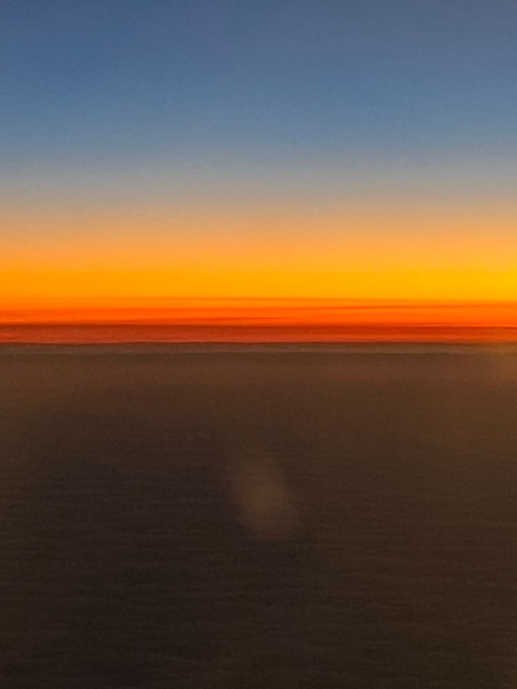The sunset from a plane window - a lighter blue segment on top of a darker blue segment split by a layer of dark to light orange 