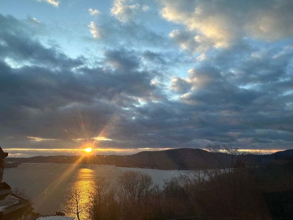 Picture of a sunset over a river with a low mountain range and blue skies with clouds 