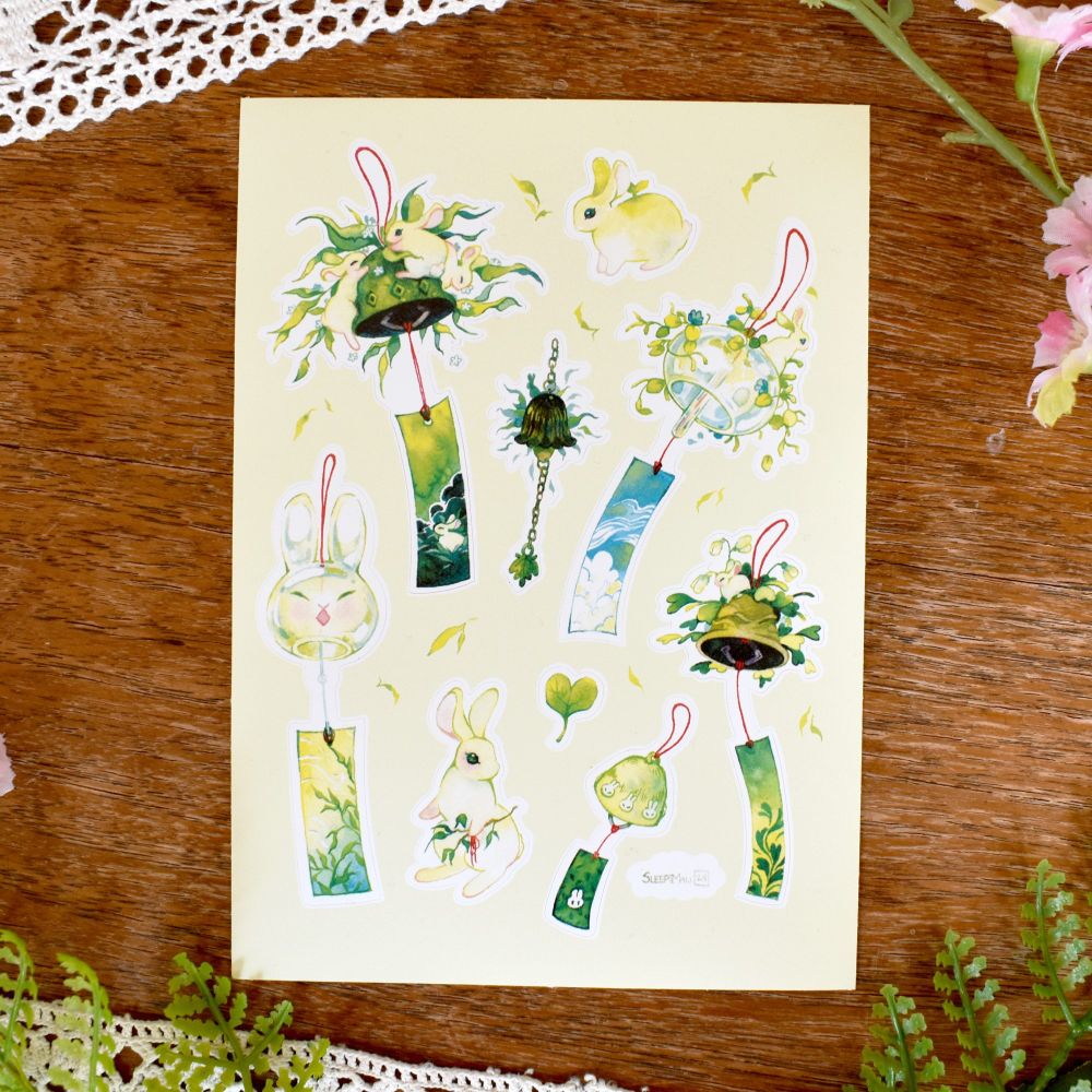 Photo of a sticker sheet of my artwork featuring bunnies and wind chimes made out of glass or ceramics 
