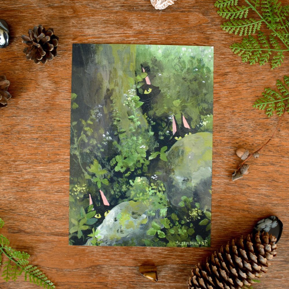 Photo of a print of an acrylic painting of three black cats' faces half poking out from behind a couple of mossy rocks and a tree in the woods