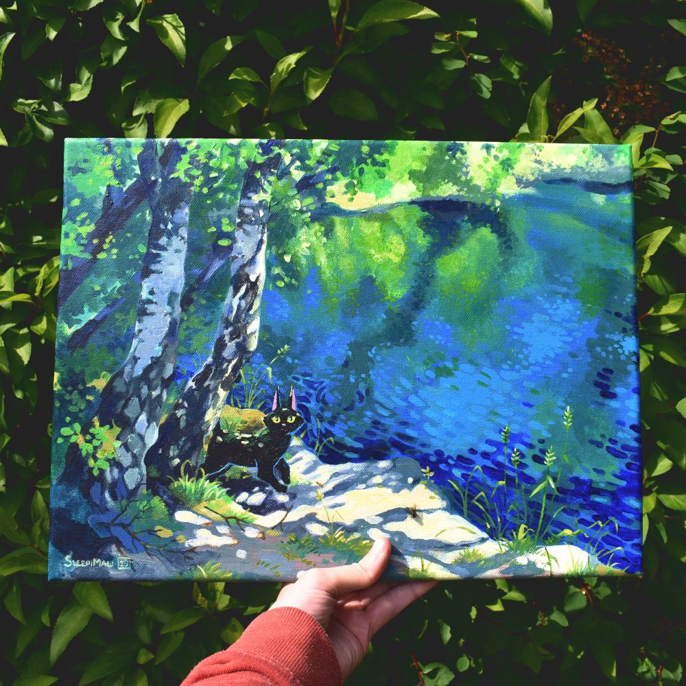 My almost blindingly pale hand holding up an acrylic painting of a black cat in dappled sunlight underneath a couple of birches by a calm lake reflecting the blue sky and greenery