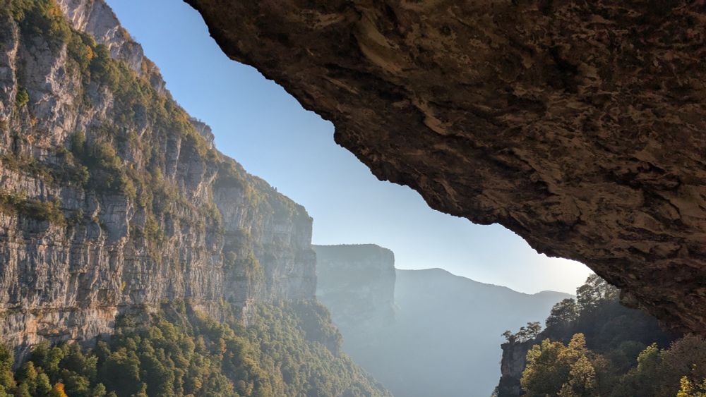 La route sous un aplomb rocheux et les gorges de la Bourne dans une brume vespérale 