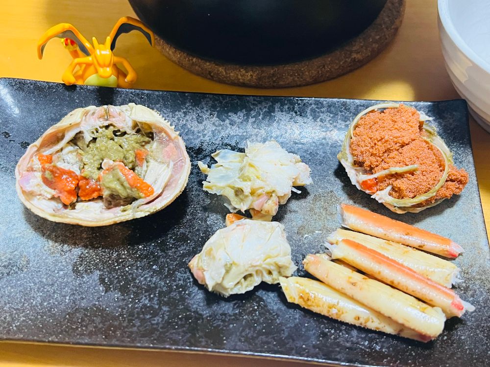 食べやすいように切り分けられた香箱カニの乗った皿とリザードンのフィギュア