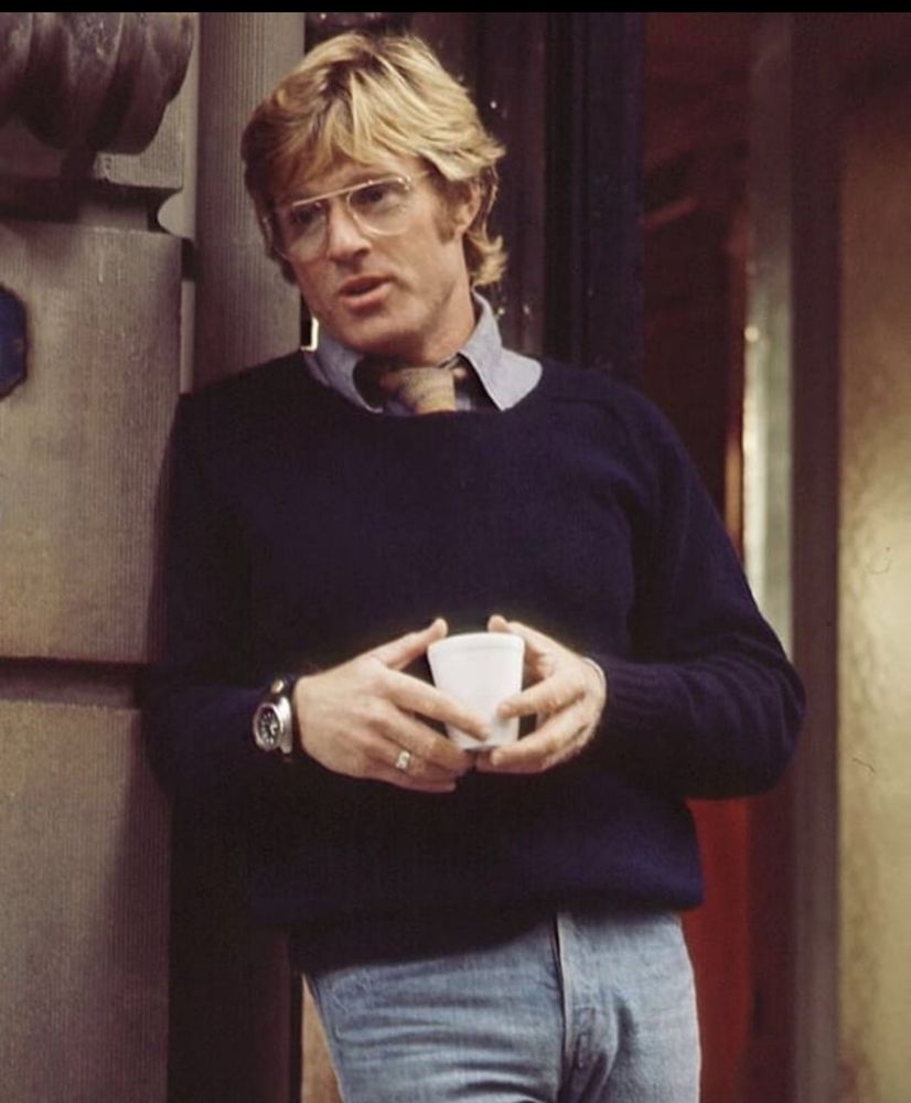 Robert Redford in a navy sweater holding a coffee cup  