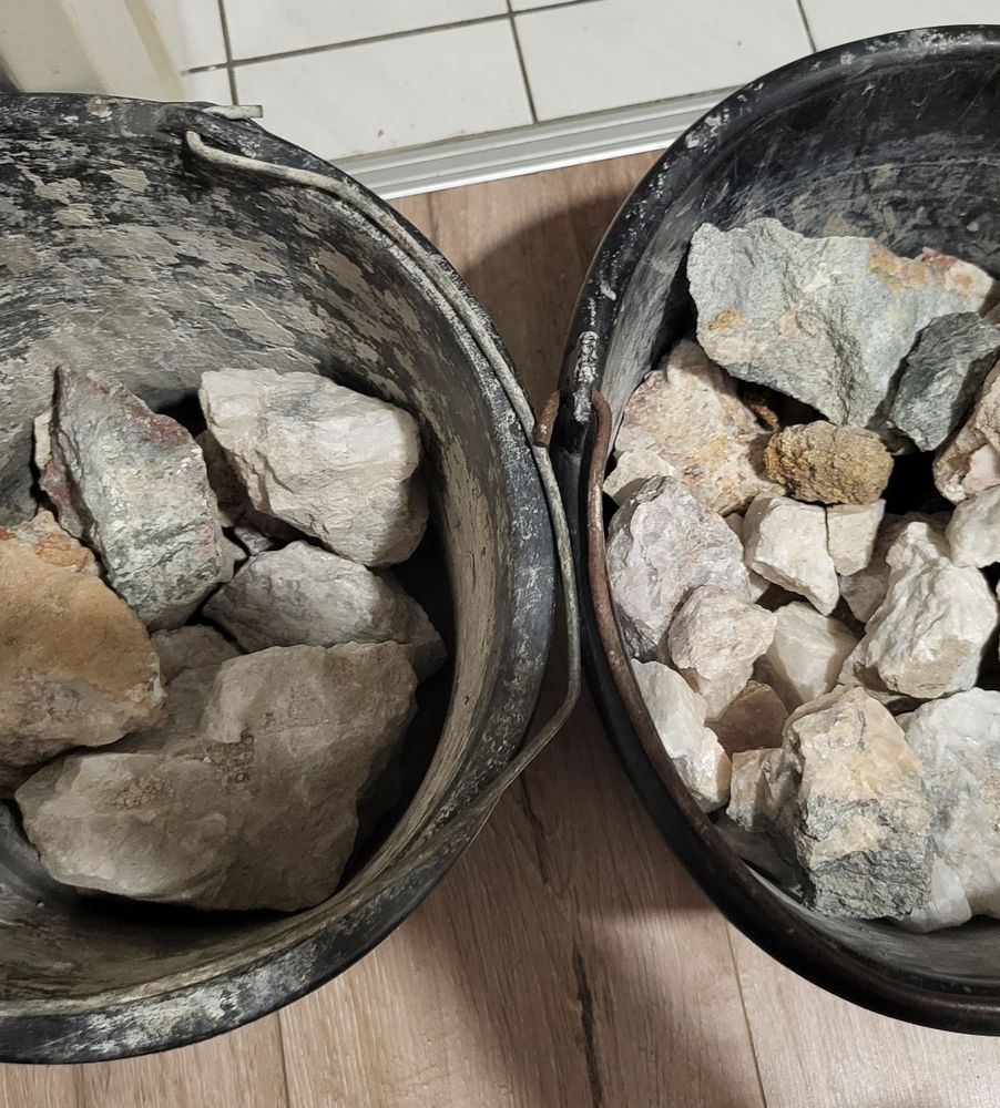 Zwei schwarze Eimer nebeneinander stehend, beide mit Mineralienbrocken verschiedester Größe gefüllt.