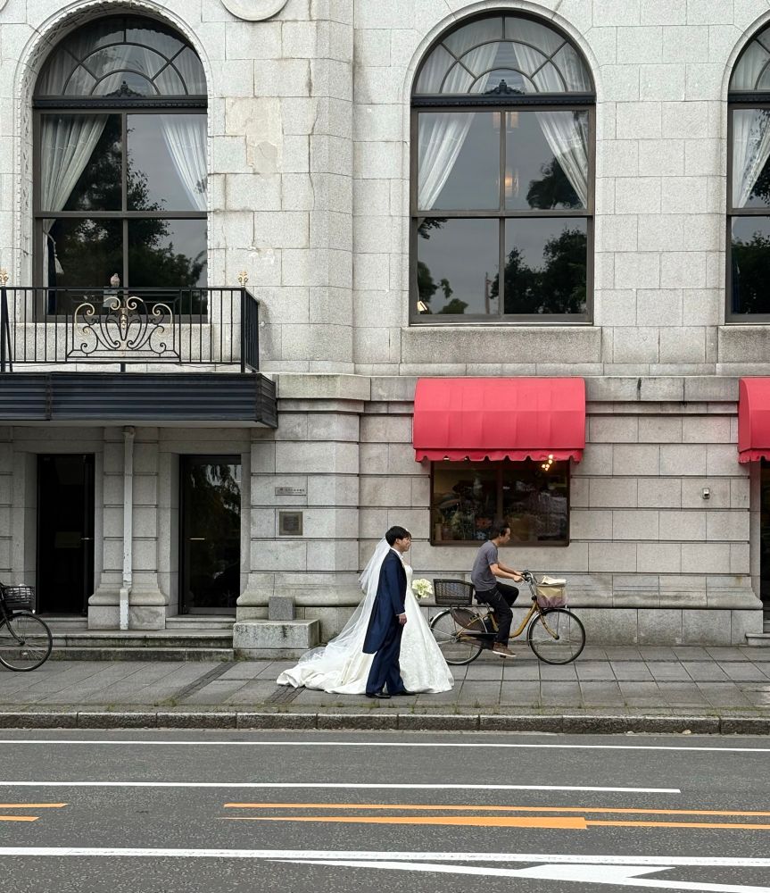 Bridge and groom pose for a photo as a man passes by on his bicycle 