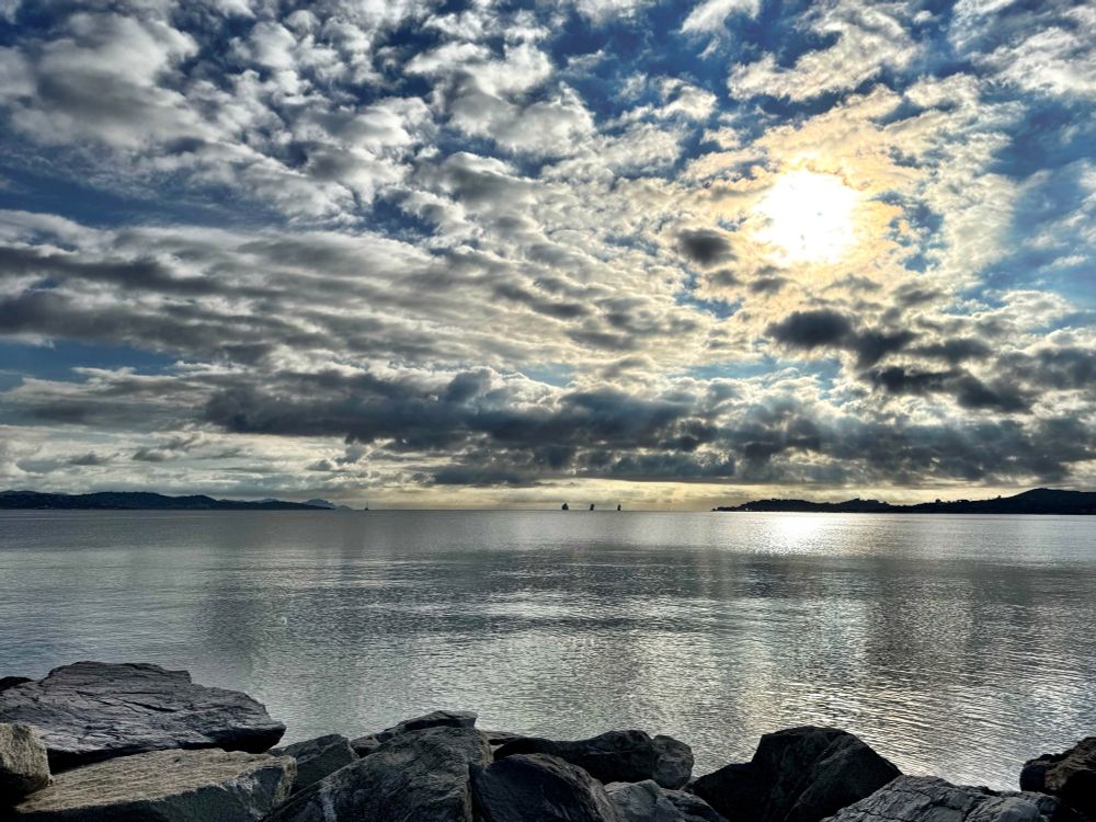 Sun breaking through scattered clouds and reflecting on the still waters of the bay below.