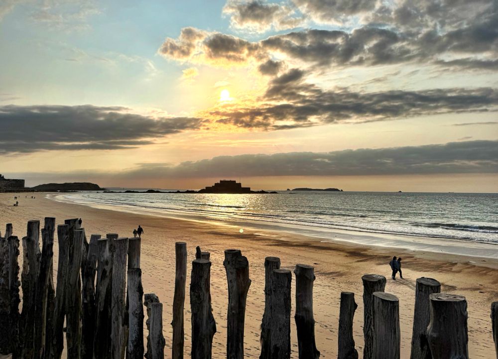 The sun dipping yellow in a golden sky of scattered cloud.  Its reflection falls over the sea below a silhouette of the tiny island fort that guards the port of Saint Malo.